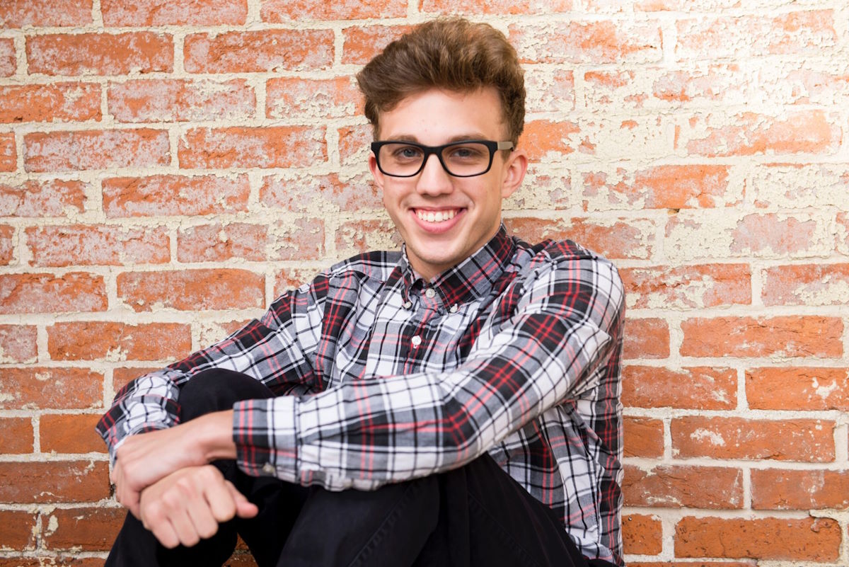 boy in glasses in front of brick wall